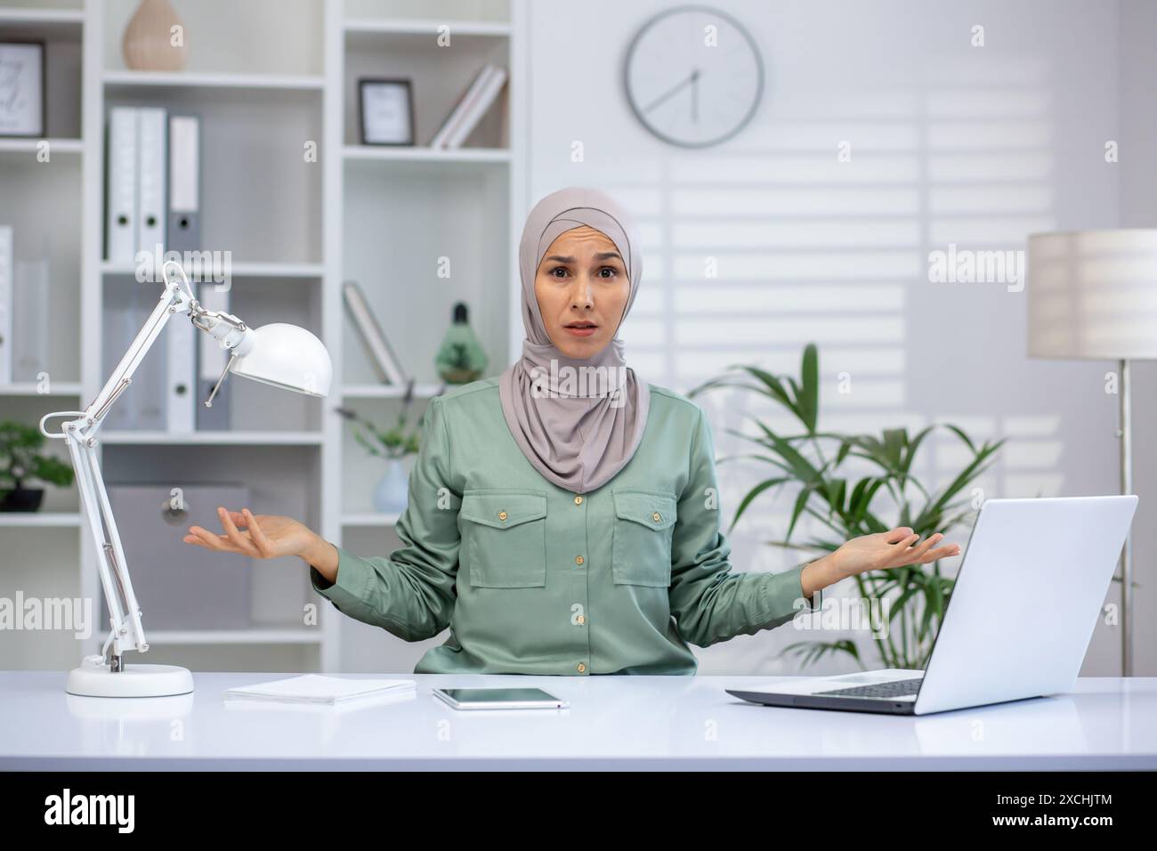 Confused businesswoman wearing hijab sitting at her desk in a modern ...