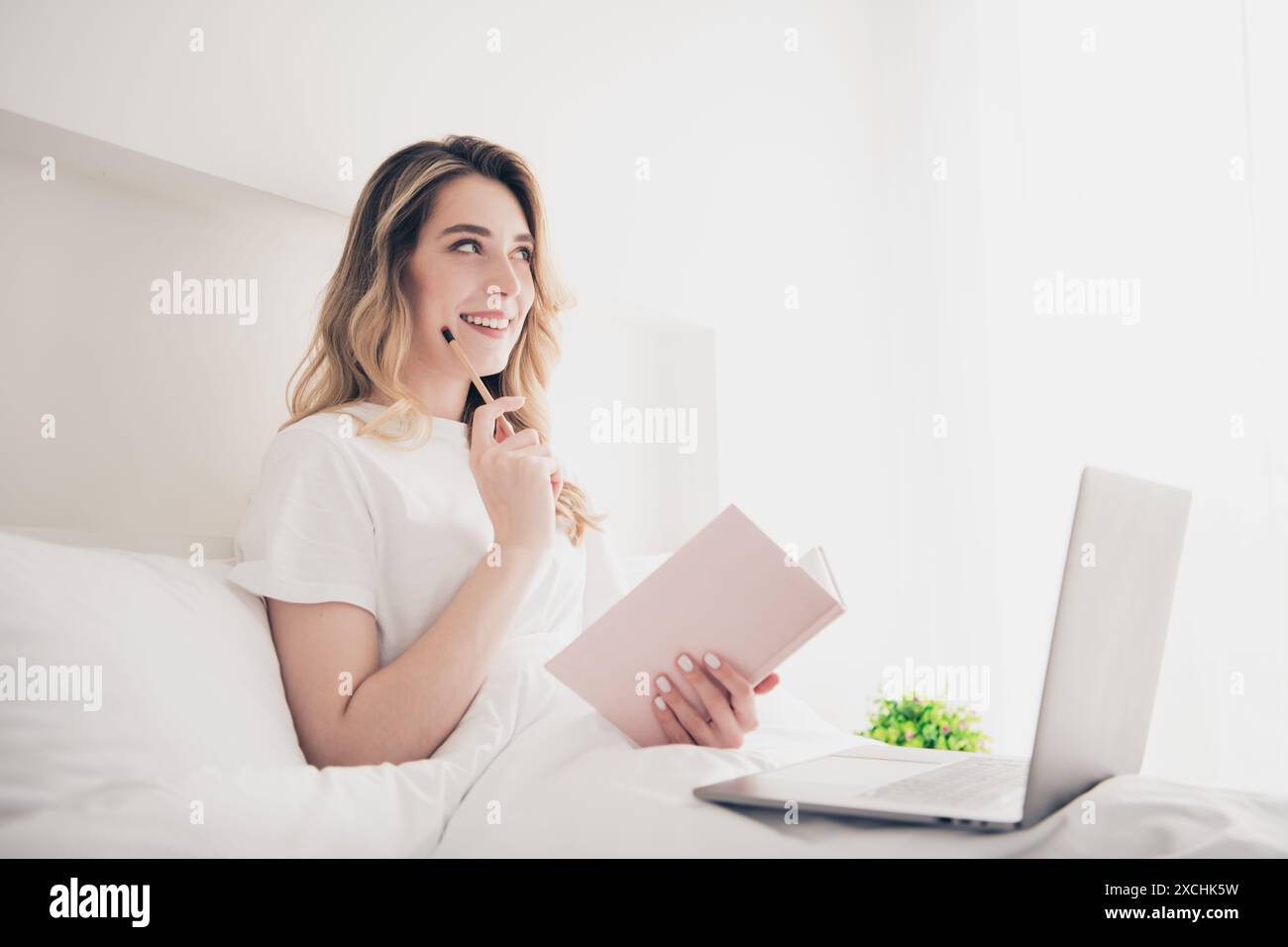 Photo of thoughtful girl lying bed writing book with netbook in bedroom ...