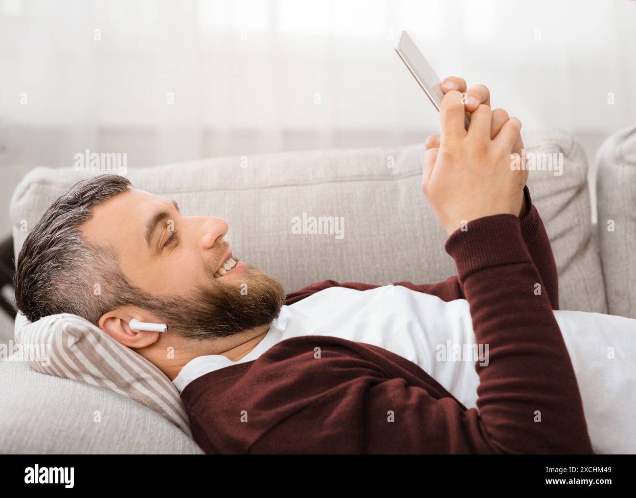 Man Smiling While Lying on Couch and Using Smartphone Stock Photo
