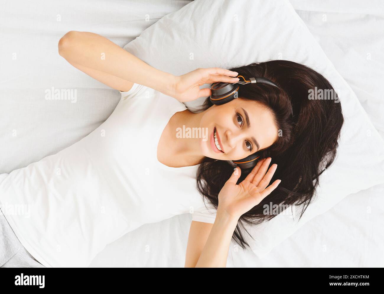 Young Lady Enjoying Music With Headphones While Lying on Bed Stock Photo