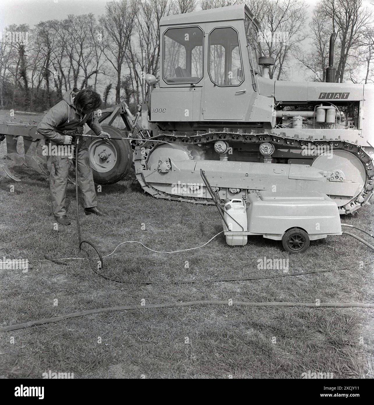 1980s, outside in a field, a man jet washing a Fiat 100C crawler tractor, England, UK. Although better known as a leading manufacturer of cars, Fiat was in fact one of the world's leading constructors of crawler tractors. Stock Photo