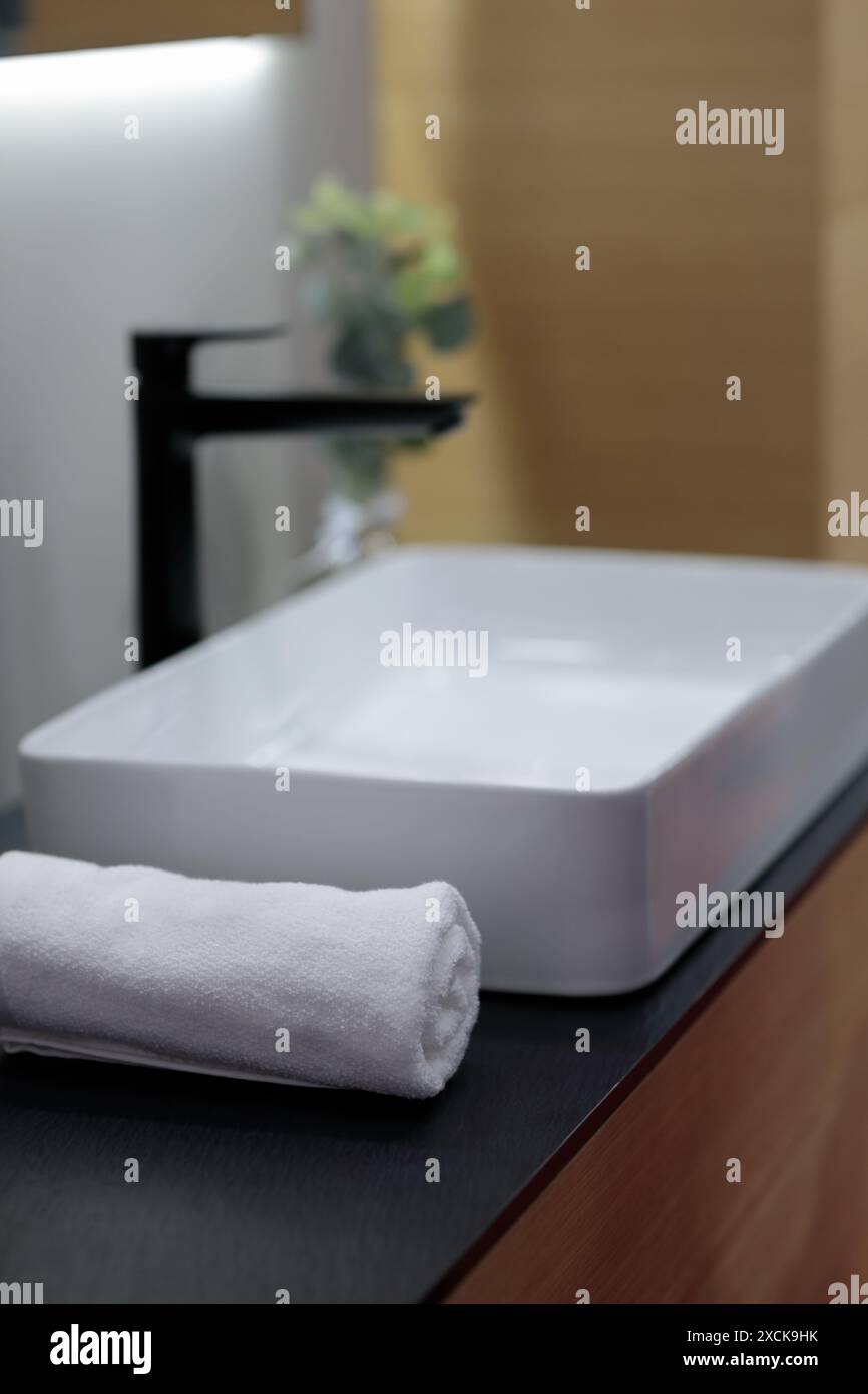 Bath towel on wooden vanity near vessel bathroom sink. Modern minimalist interior design. Selective focus. Stock Photo