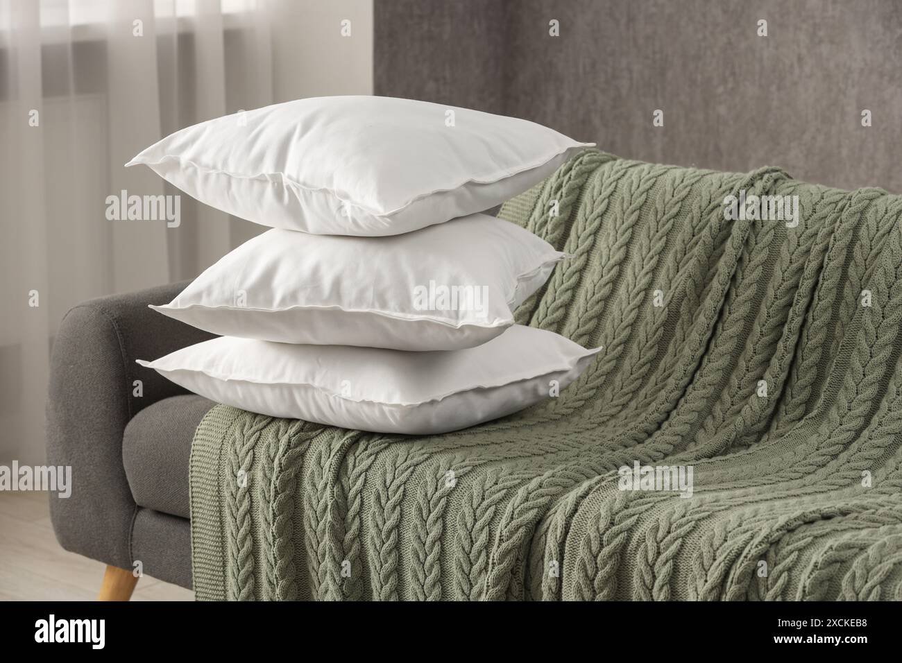 Stack of soft white pillows on sofa and blanket indoors Stock Photo