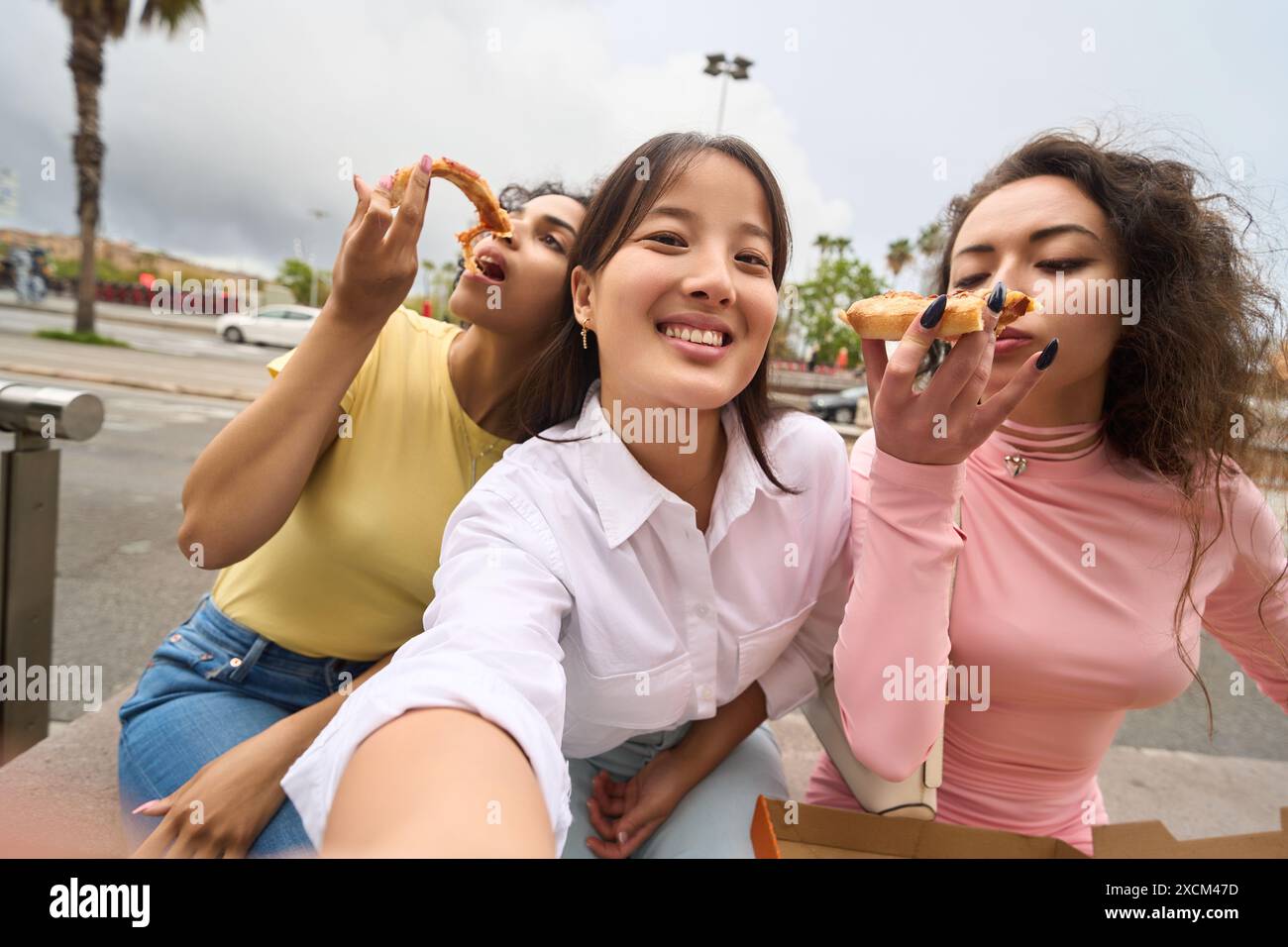 Three women are eating pizza and smiling Stock Photo