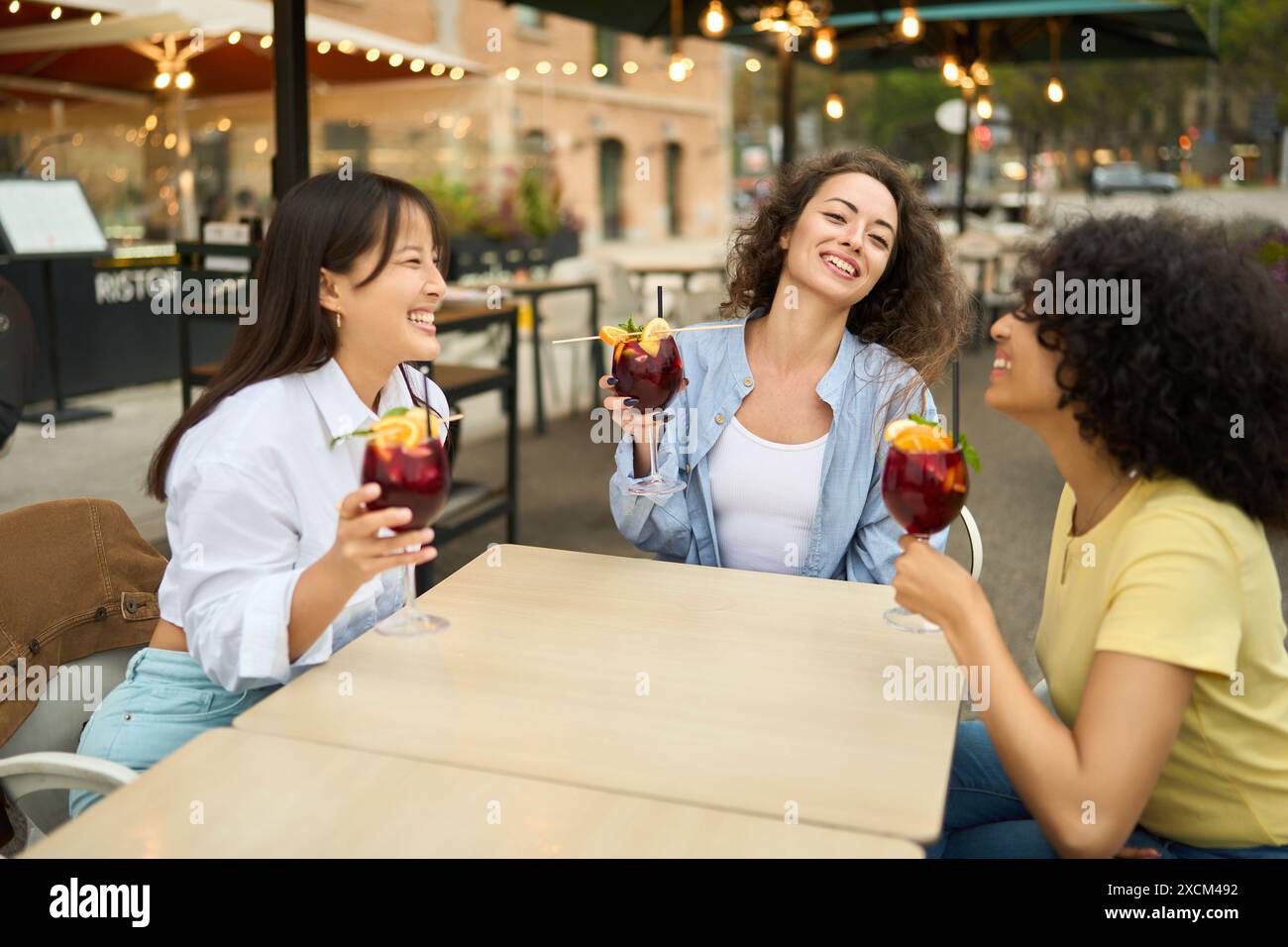 Three women are sitting at a table with drinks and smiling Stock Photo