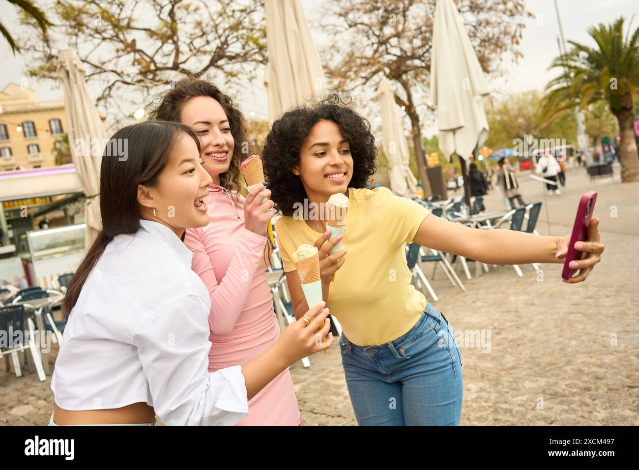 Three young women enjoying ice cream and taking selfies Stock Photo