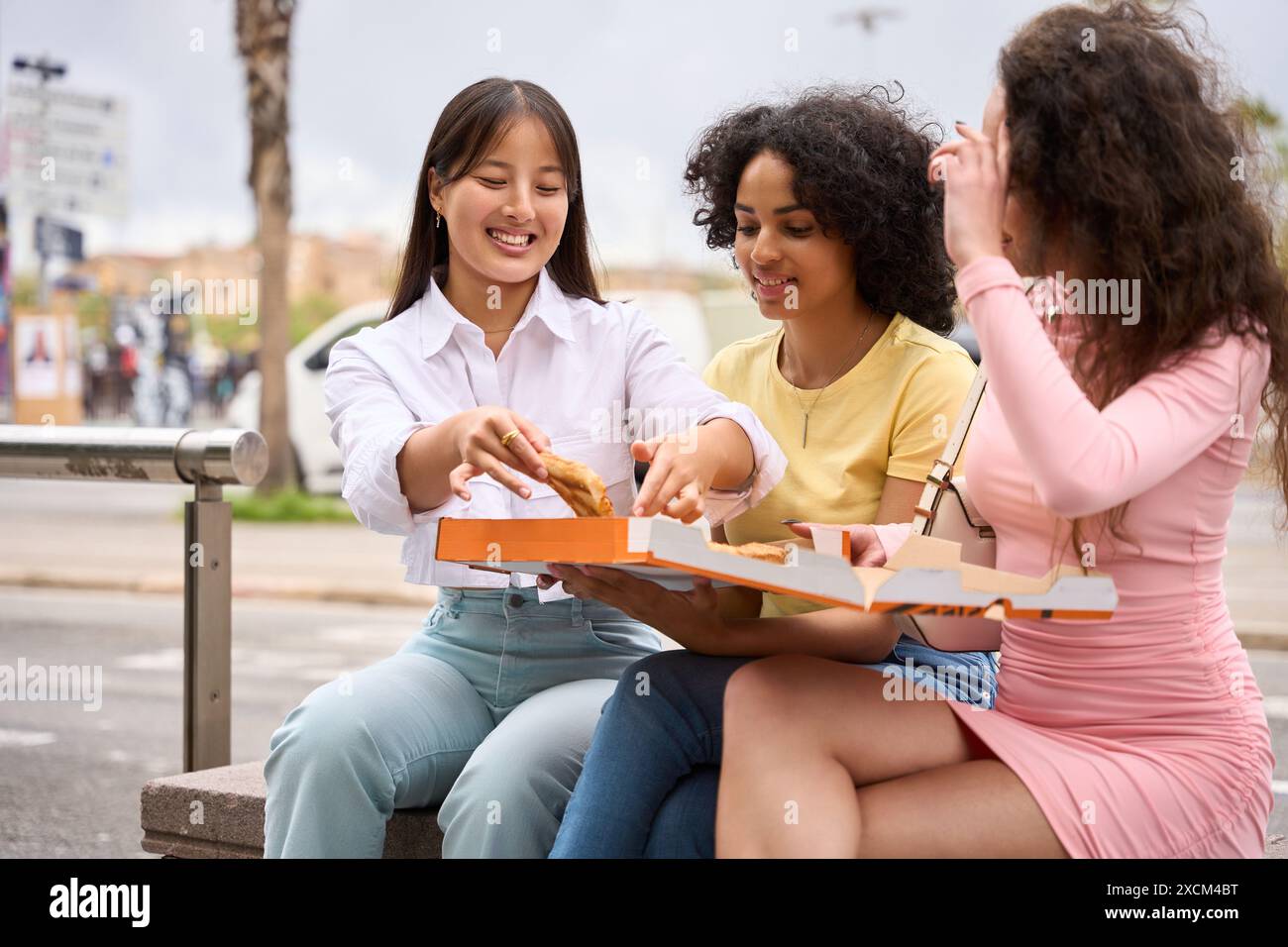 Three young multiethnic women sharing pizza outdoors Stock Photo