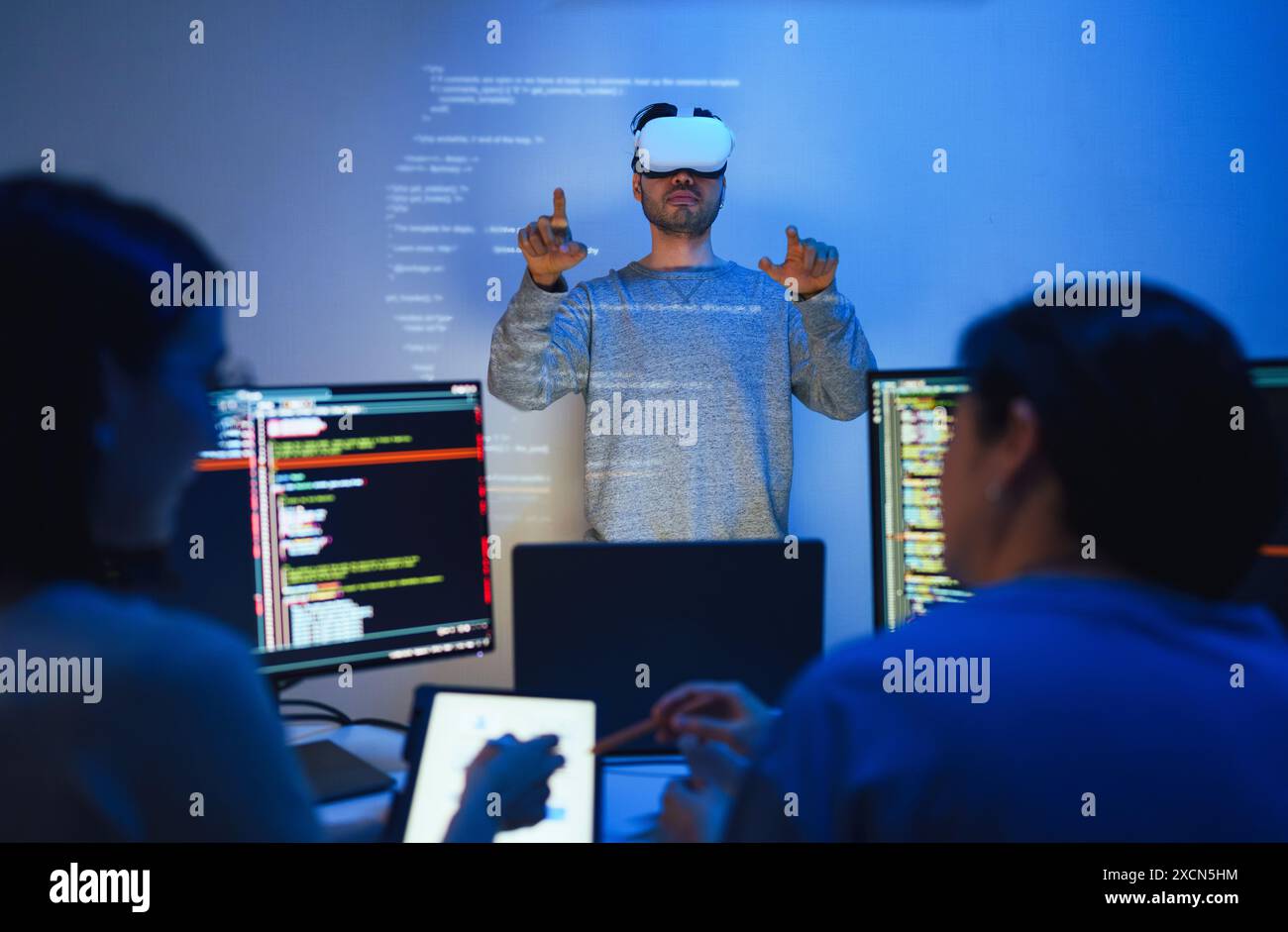 developer uses a VR headset to interact with projected interface designs, while colleagues discuss and code on screens, highlighting the integration o Stock Photo