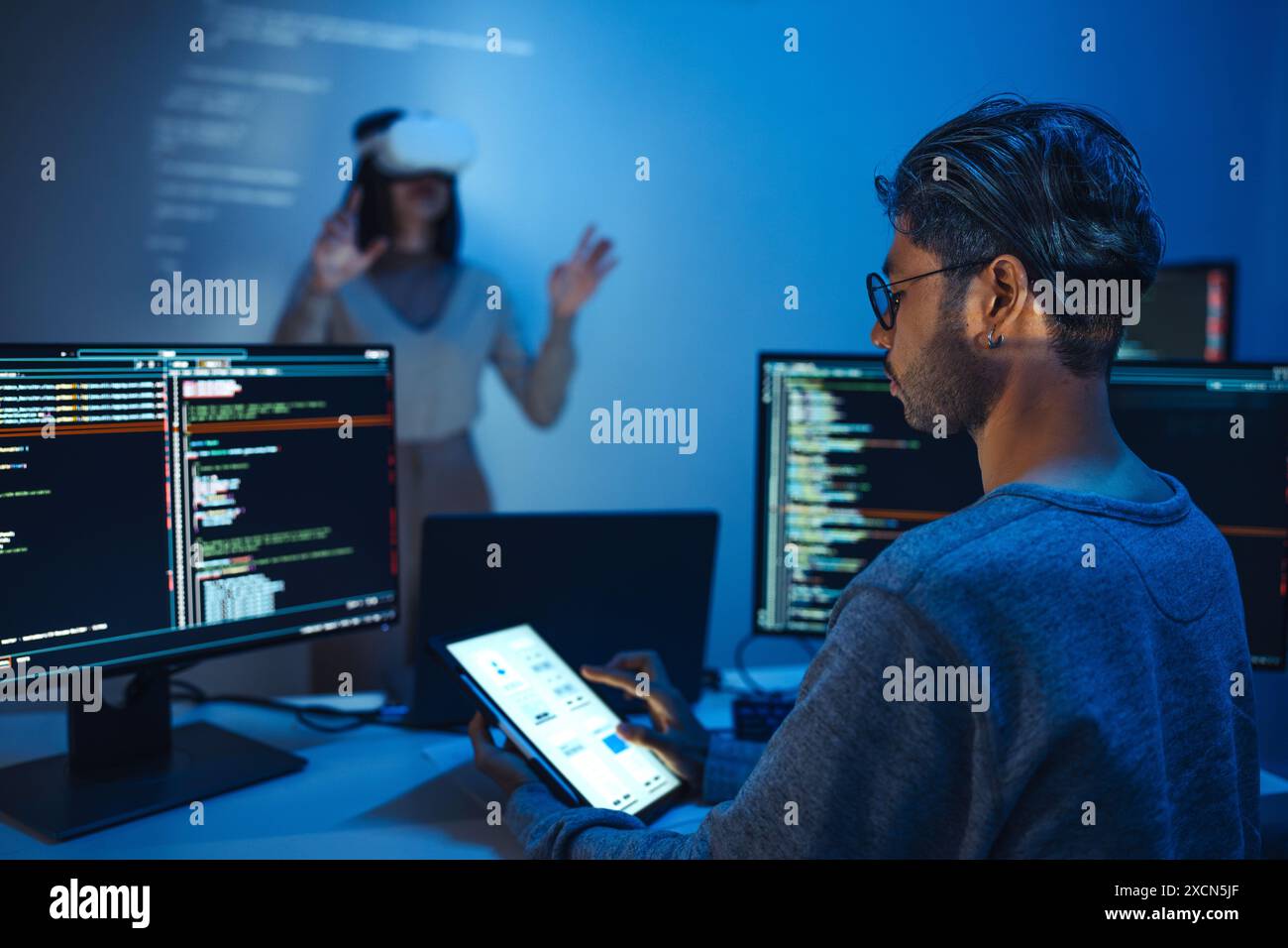 developer uses a VR headset to interact with projected interface designs, while colleagues discuss and code on screens, highlighting the integration o Stock Photo