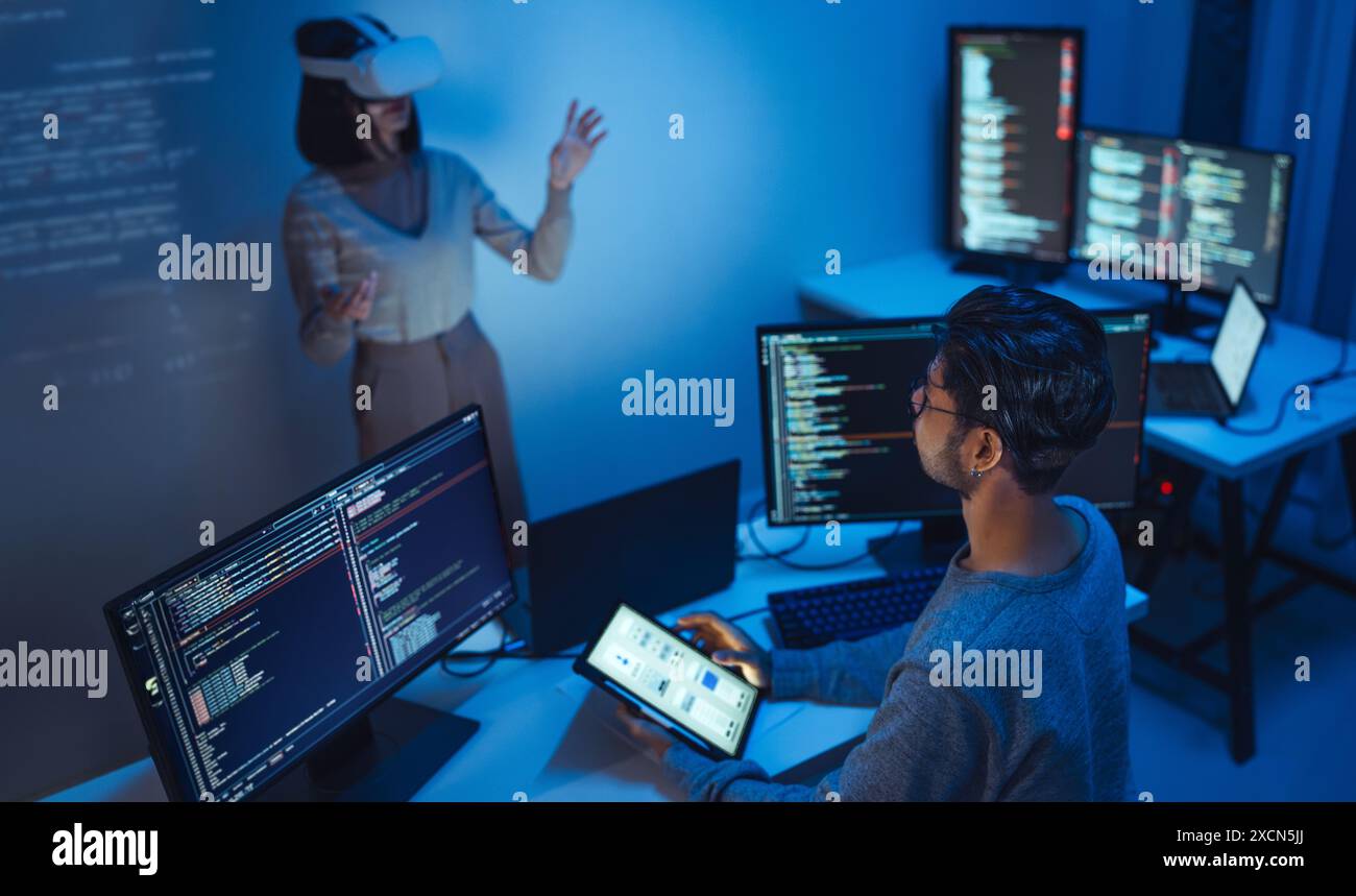 developer uses a VR headset to interact with projected interface designs, while colleagues discuss and code on screens, highlighting the integration o Stock Photo