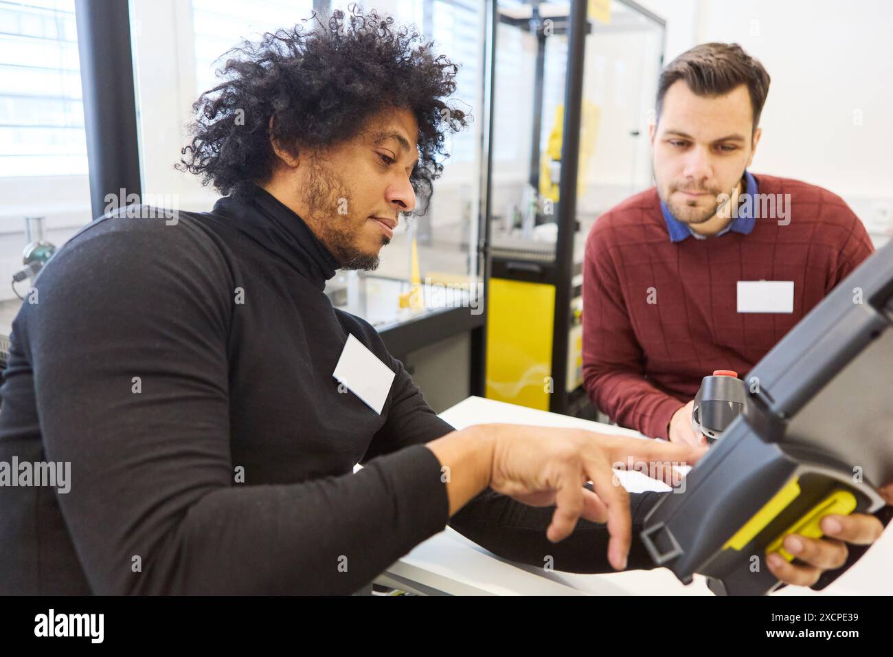 Two engineers engaged in programming a robotic system with a gripper arm, focusing on industrial automation and robotics training in a workshop settin Stock Photo