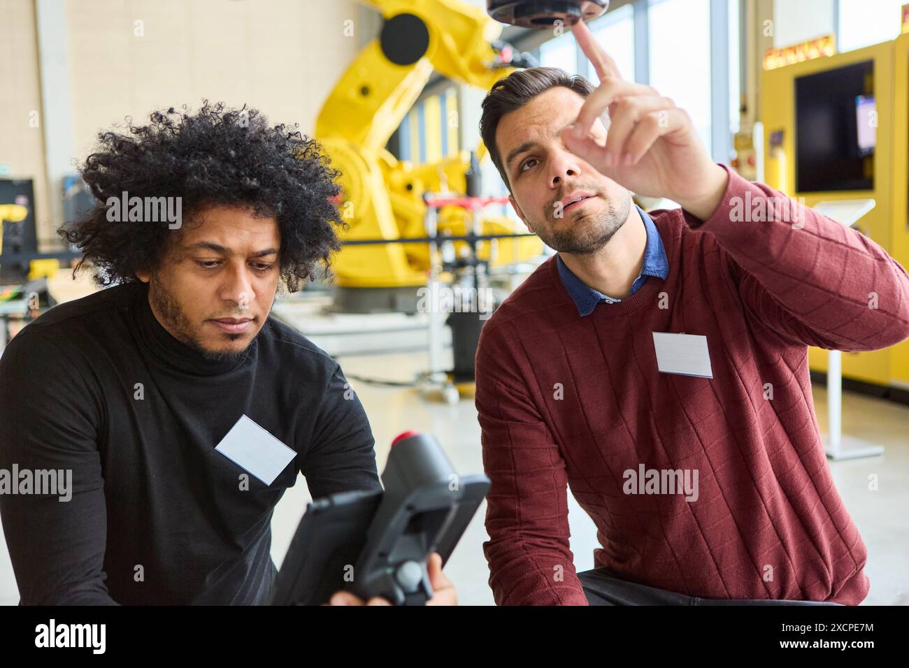 Two engineers collaborate on programming a robotic arm in an industrial ...