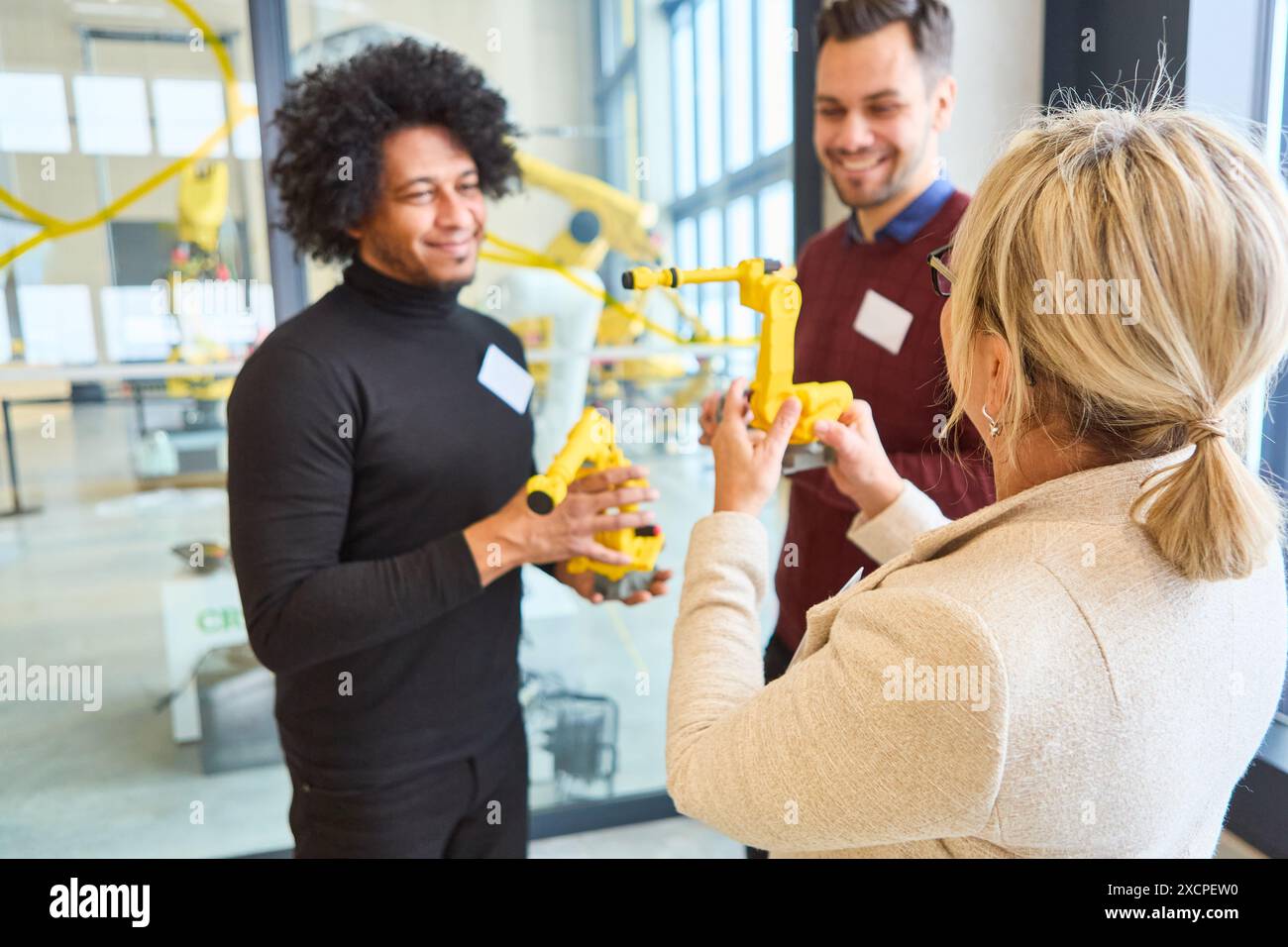 Three engineers collaborate in a workshop, discussing and examining a robotic gripper arm. They are focused on programming and process automation for Stock Photo