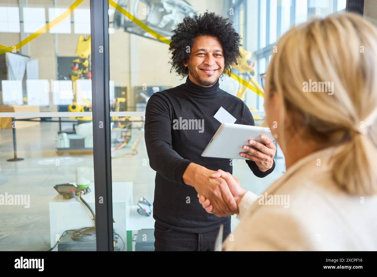 A friendly business meeting in a robotics lab featuring a handshake and smile, highlighting collaboration in technology and robotics. Stock Photo