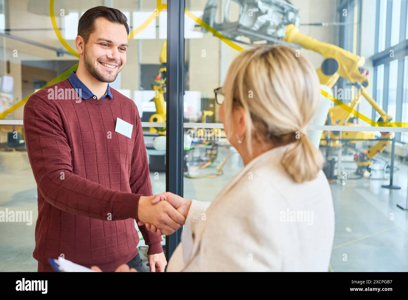 Business professionals shaking hands at a robotics training facility, highlighting technology and industrial automation. Background shows robotic arms Stock Photo
