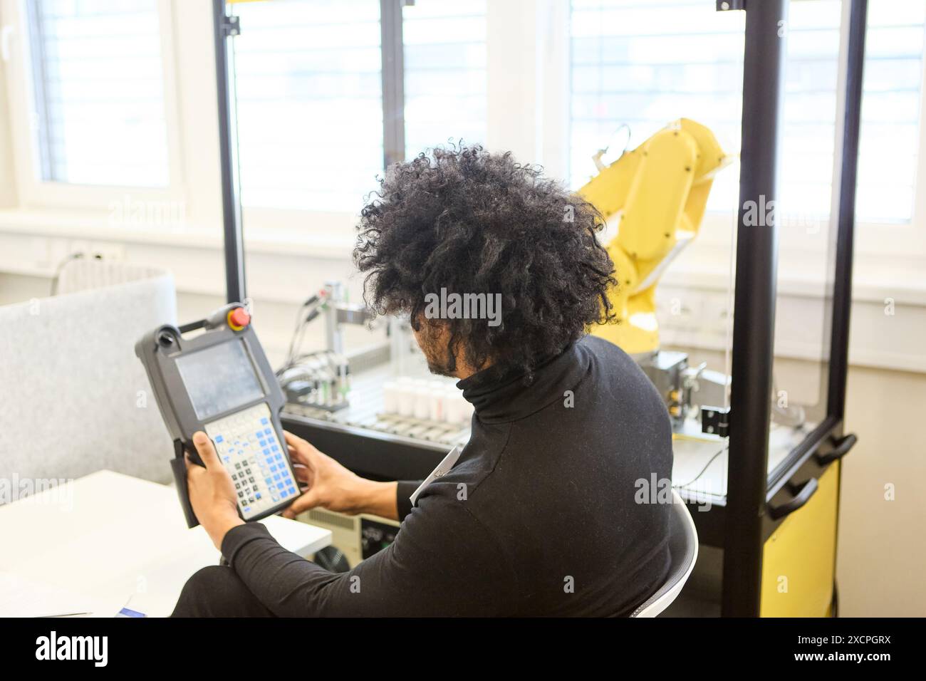 Engineer working on programming an industrial robot using a control panel in a modern laboratory setting. Stock Photo
