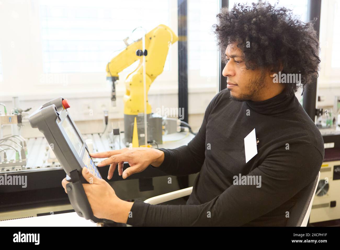 Male engineer using a control panel to program an industrial robot with a gripper arm for automated production in a modern factory setting. Stock Photo