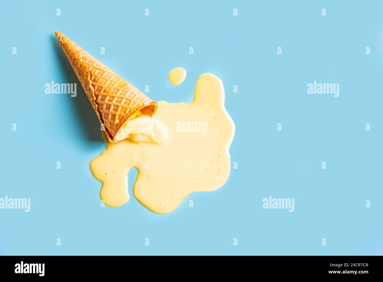 Ice cream waffle cone with melted yellow mango ice cream on pastel blue background. Minimalistic creative summer food concept design. Stock Photo