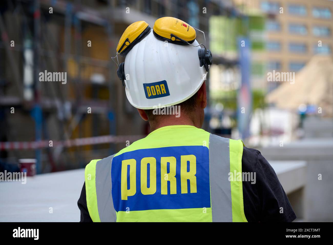 Ein Arbeiter der Firma Porr in Rückenansicht auf einer Baustelle. Er trägt eine gelbe Warnweste und einen weißen Helm mit Gehörschutz. Veröffentlichun Stock Photo