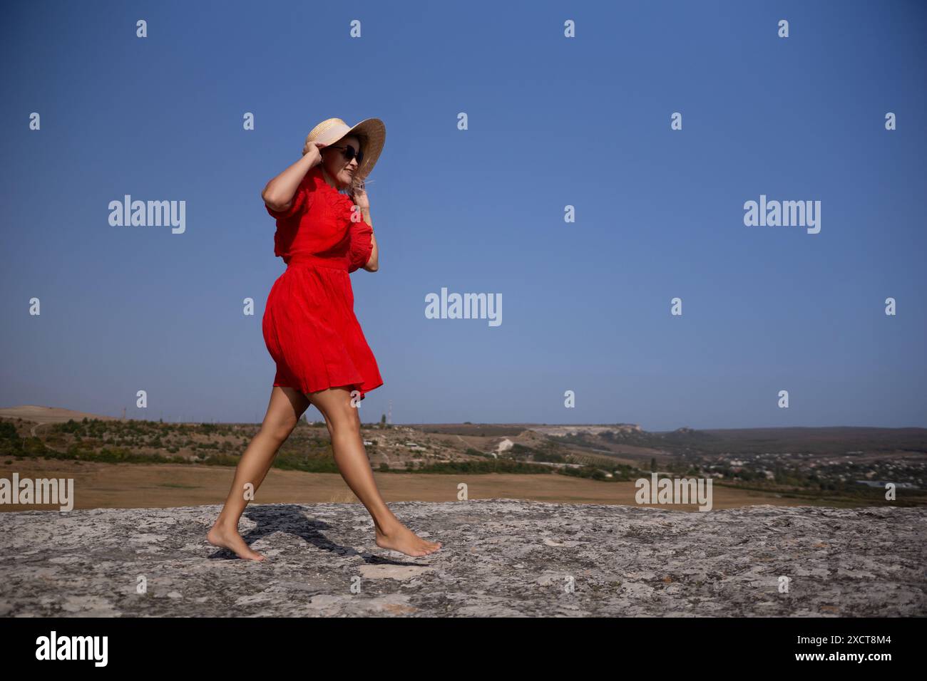 A woman in a red dress is walking barefoot on a rocky hillside Stock ...
