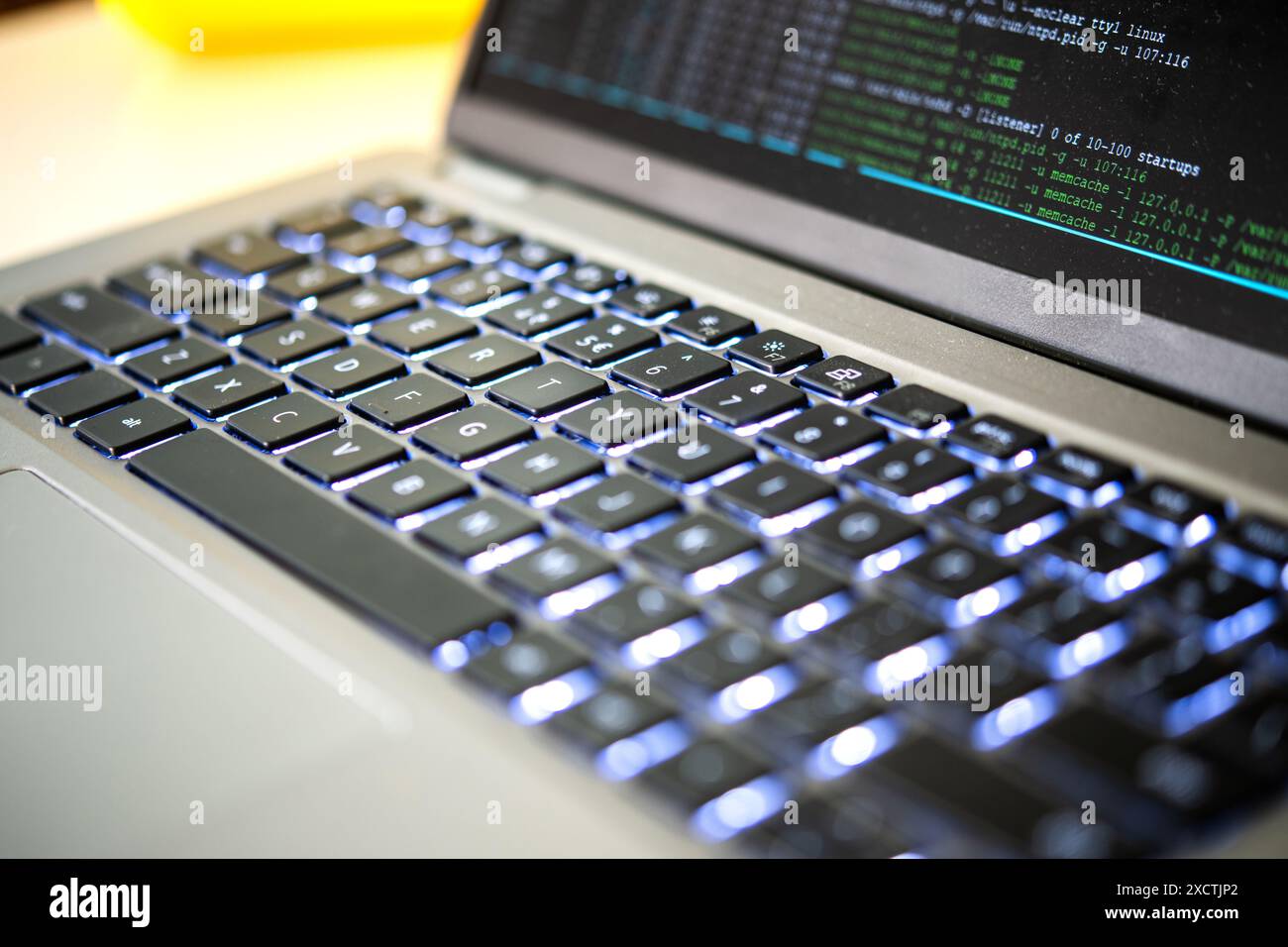 Capture of a modern laptop's illuminated keyboard, with visible programming code on screen, emphasizing advanced technology, hacking, data brach, ddos Stock Photo