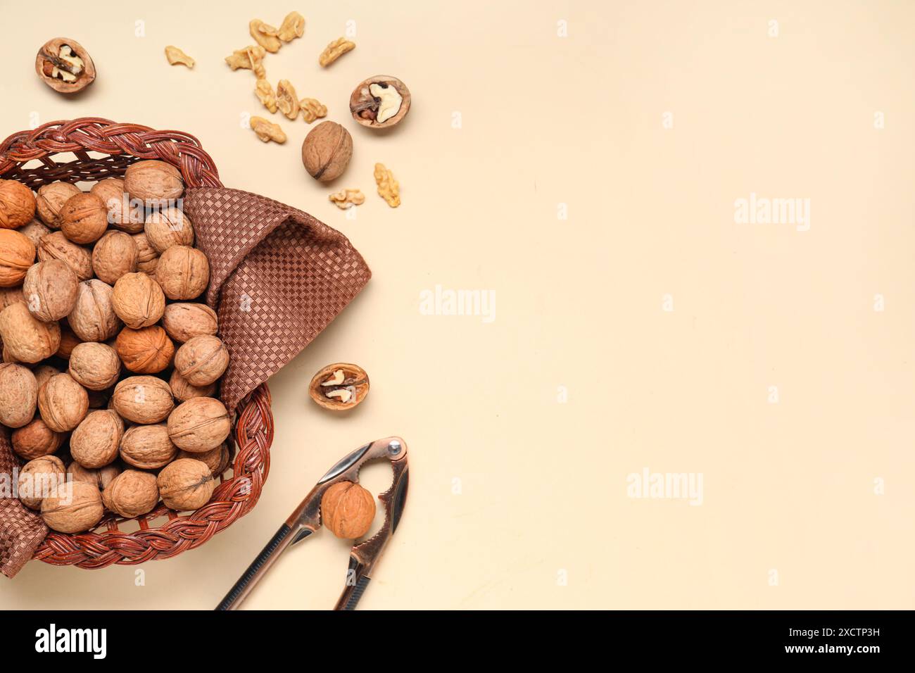 Wicker basket with walnuts and nutcracker on yellow background Stock Photo
