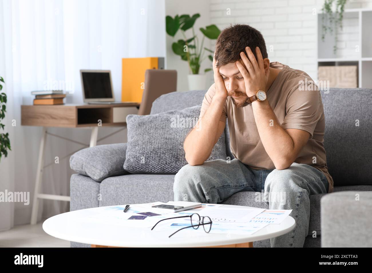Stressed young man in debt sitting on sofa at home Stock Photo - Alamy