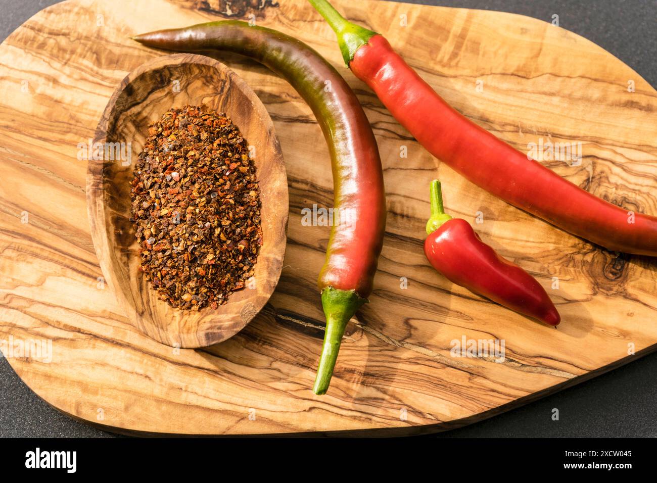 Chilli peppers and crushed chilli peppers on a wooden board Stock Photo