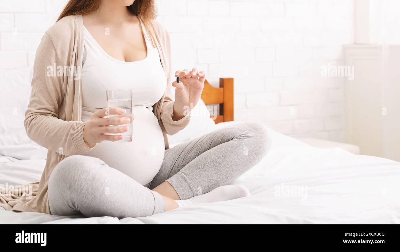 Pregnant Woman Sitting on Bed With Glass Water and Pill Stock Photo