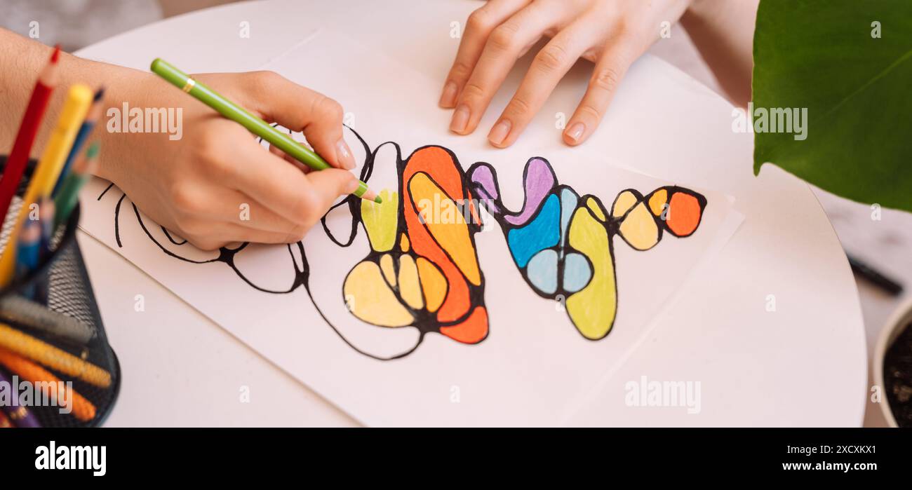 Lady paints over a drawing on a white sheet with colored pencils Stock Photo