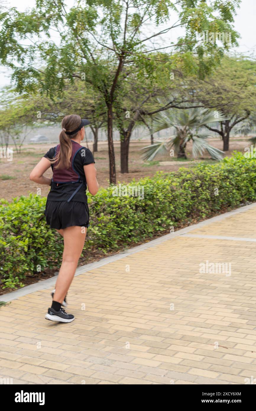 Woman running on a paved path in a park surrounded by trees and ...