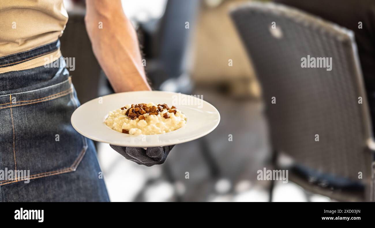The waiter is holding a plate with traditional Slovak bryndza dumplings. Original name - Bryndzove halusky. Stock Photo