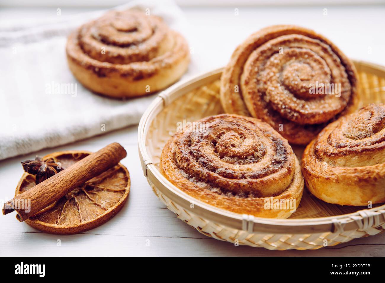 Freshly baked homemade cinnamon rolls with sugar on top in basket in home kitchen on white table, cinnamon stick for decoration. Selective focus. Stock Photo