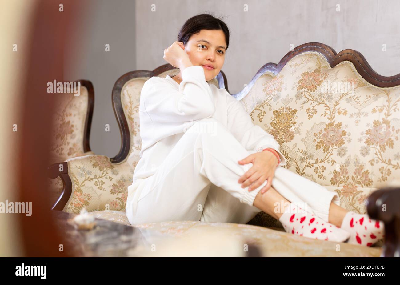 Relaxed young brunette sitting on soft antique sofa at home Stock Photo