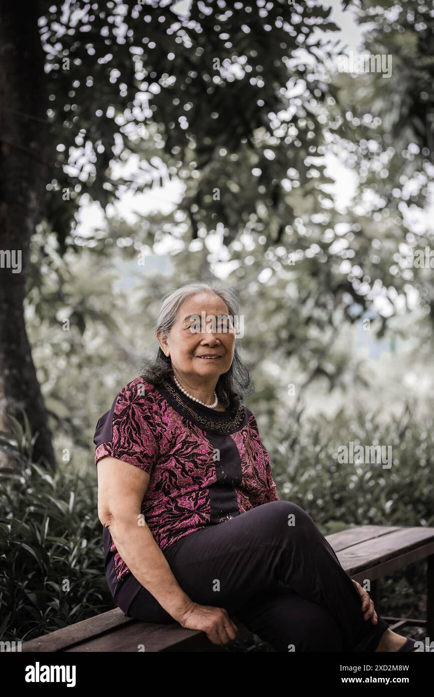 Elderly woman at the park. Asian Senior woman sitting on a bench in a summer park. Old smiling lady sits on a park bench in Vinh Minh Vietnam-May 31,2 Stock Photo