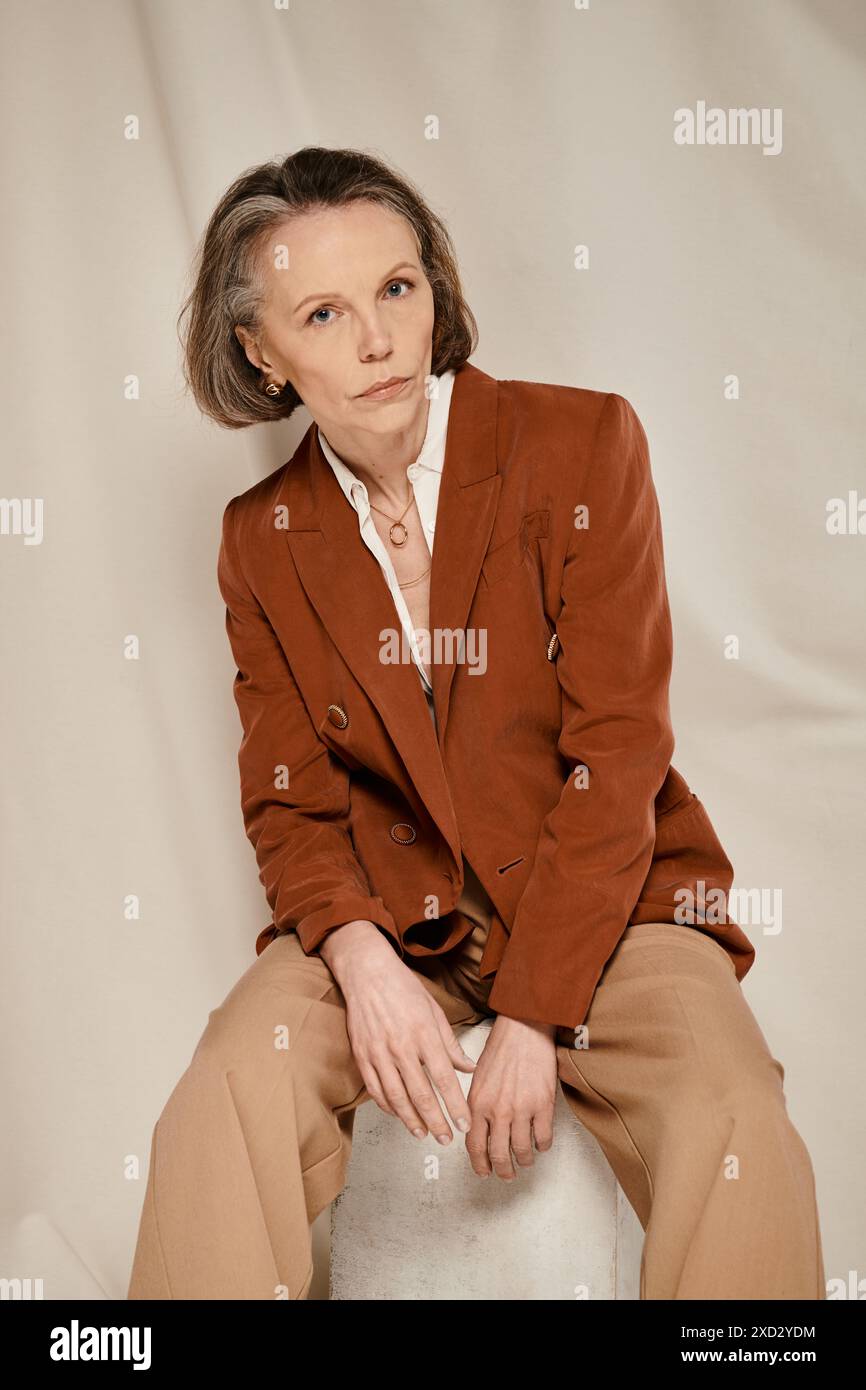 Stylish mature woman in brown blazer and tan pants sitting comfortably ...