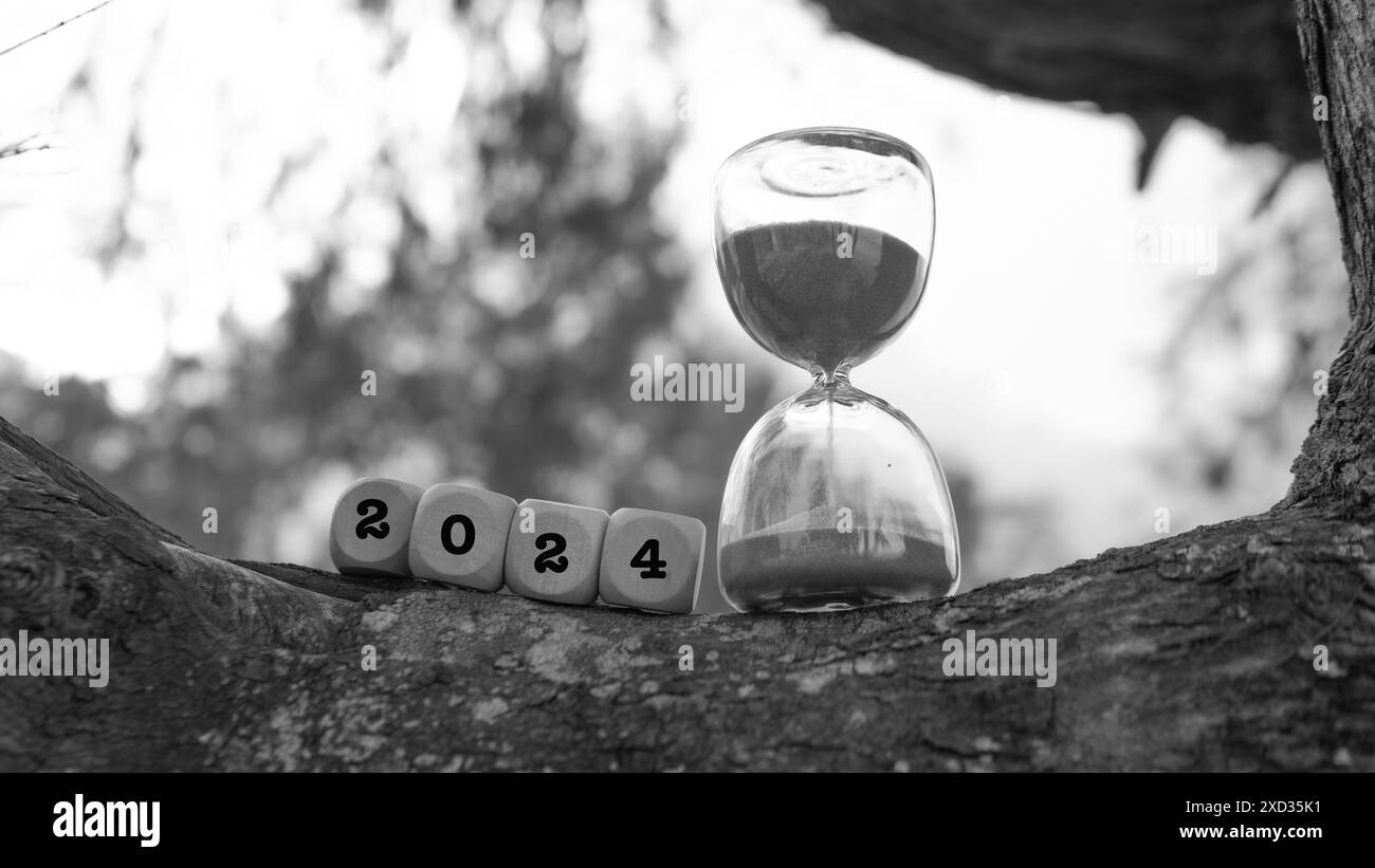 Black and white picture with a square dice shaped with hour glass and a text of 2024. Showing the end of the year 2024 Stock Photo