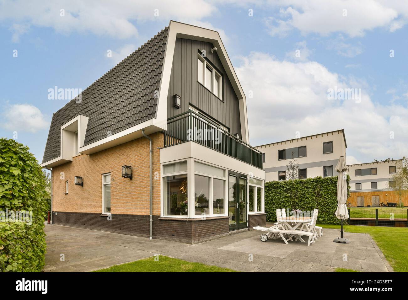 A house with a lawn in the front and two chairs on the outside, all facing towards each other buildings Stock Photo