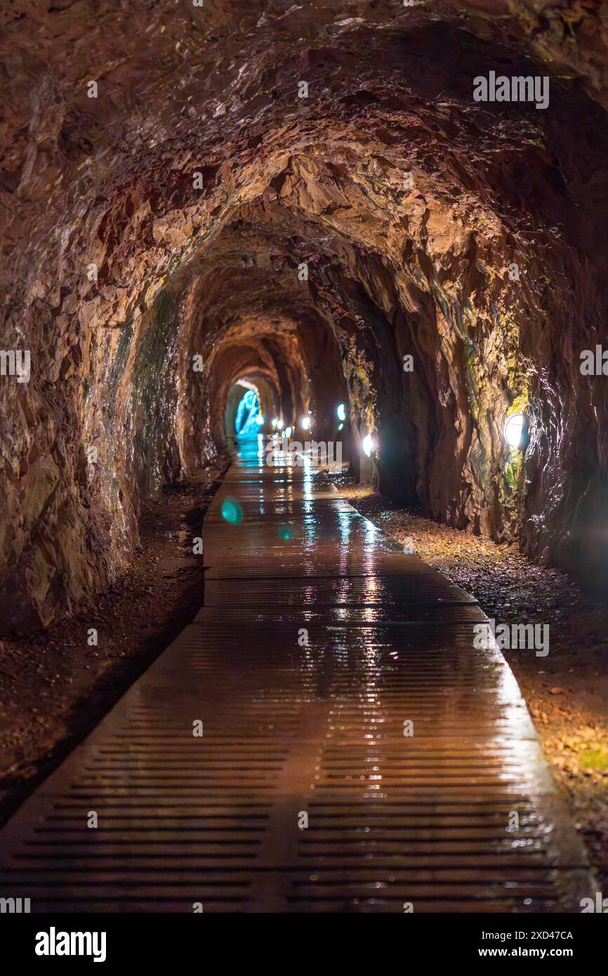 A long tunnel with a wet floor. The tunnel is dark and the lights are on. The water on the floor makes it slippery Stock Photo