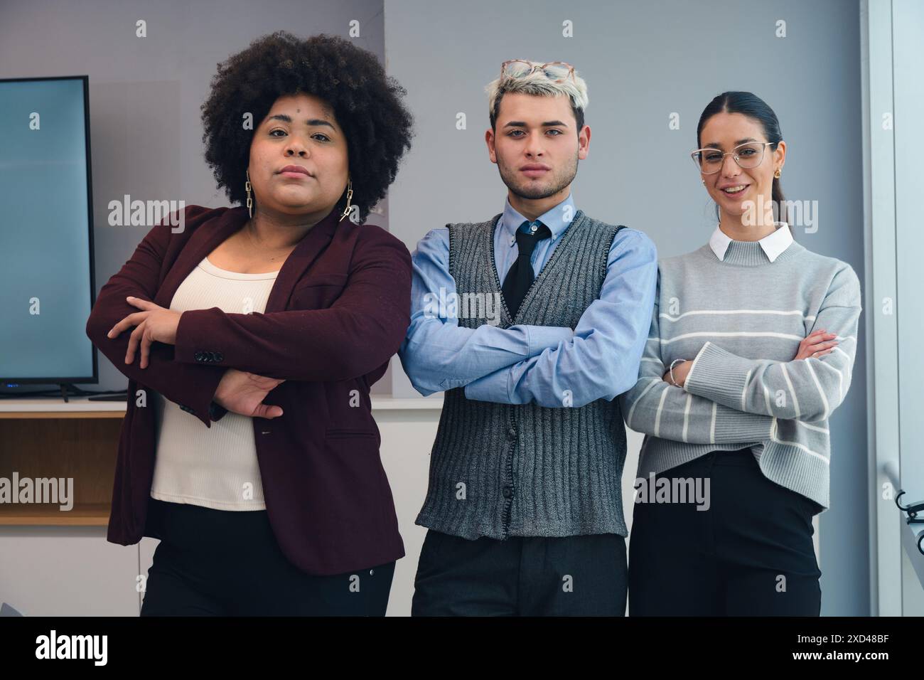 Portrait of three business people are together in the office looking at the camera with their arms crossed, they represent seriousness and commitment Stock Photo
