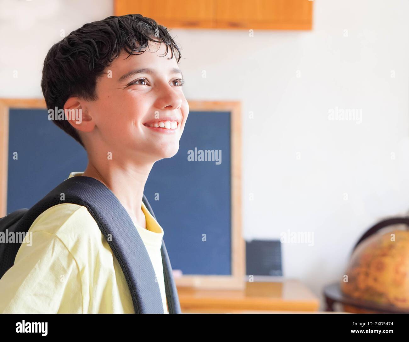 preteen boy happy and excited about going back to school, with a backpack and globe in the background. Stock Photo