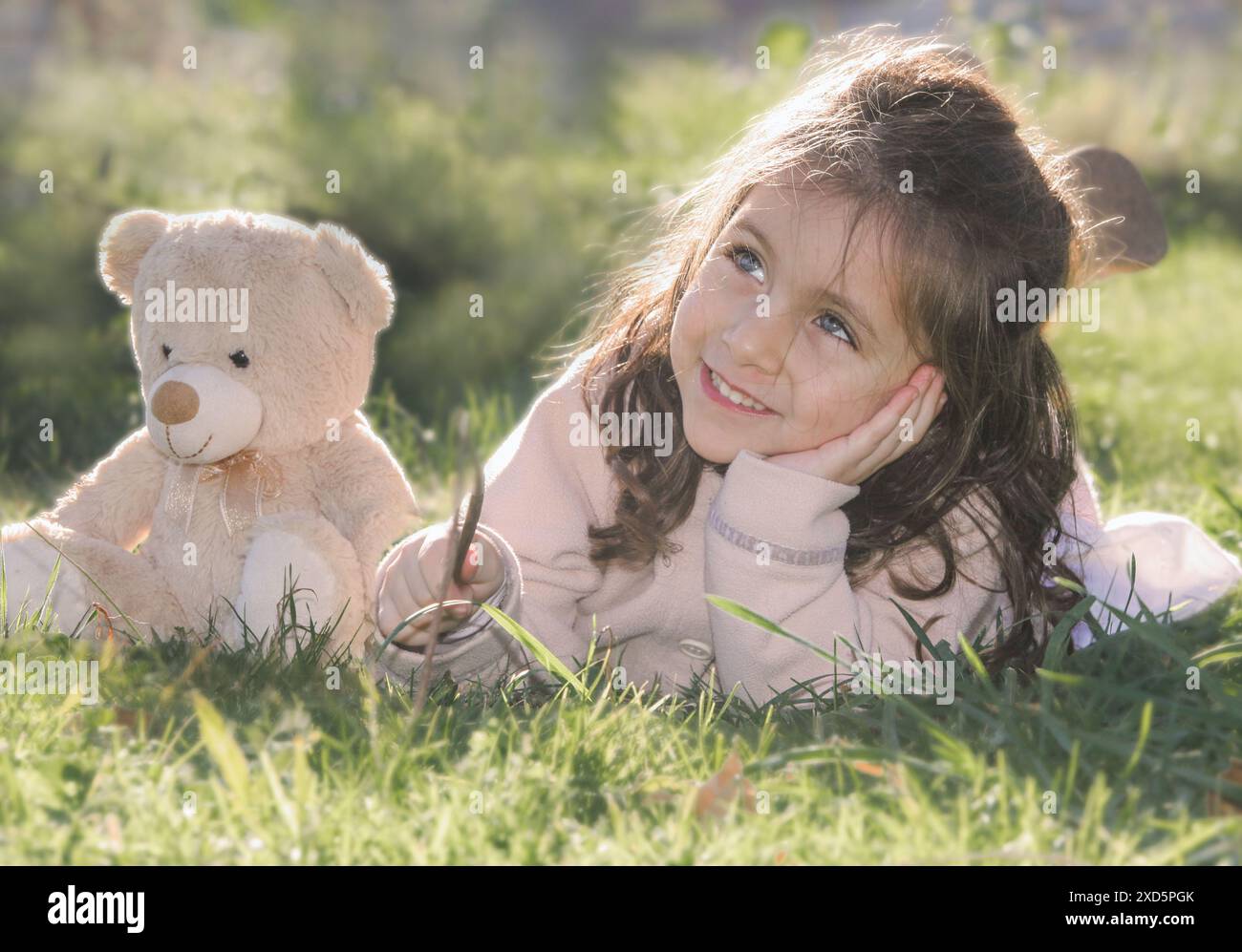 cheerful little girl with  teddy bear lying on grass Stock Photo