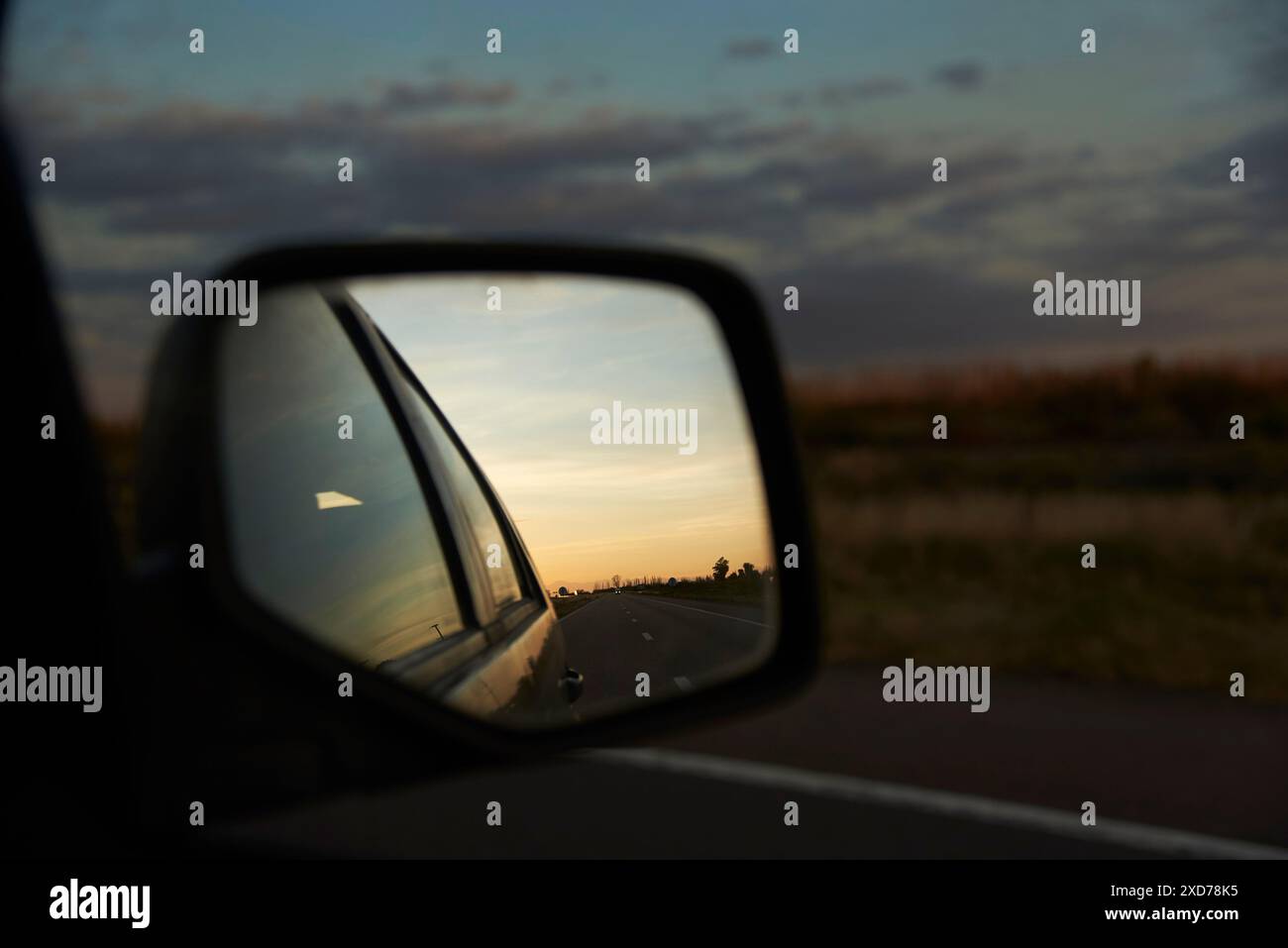 Rear view mirror of a traveling vehicle, in the reflection you can see the road at twilight. Concept: the end of the journey, returning home after a c Stock Photo