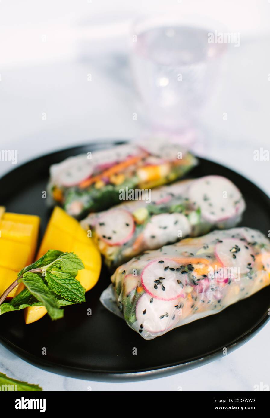 Three fresh spring rolls on a black plate with mango slices Stock Photo