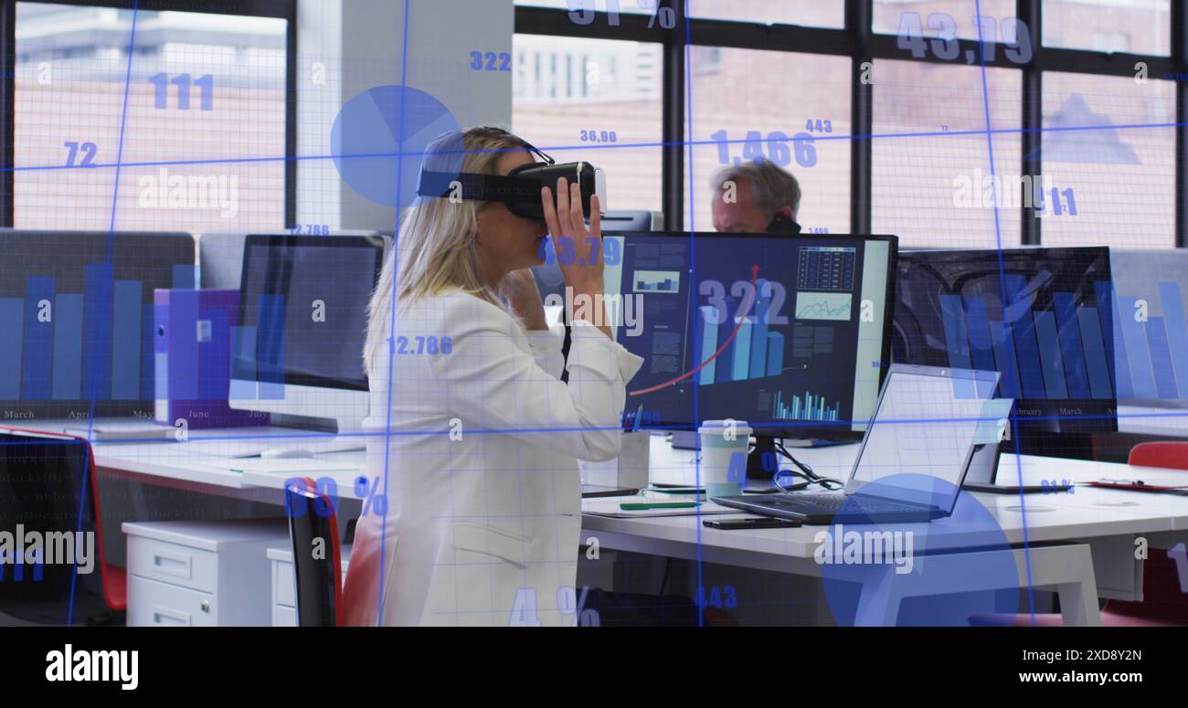 Image of statistical data processing against caucasian woman wearing vr headset at office Stock Photo