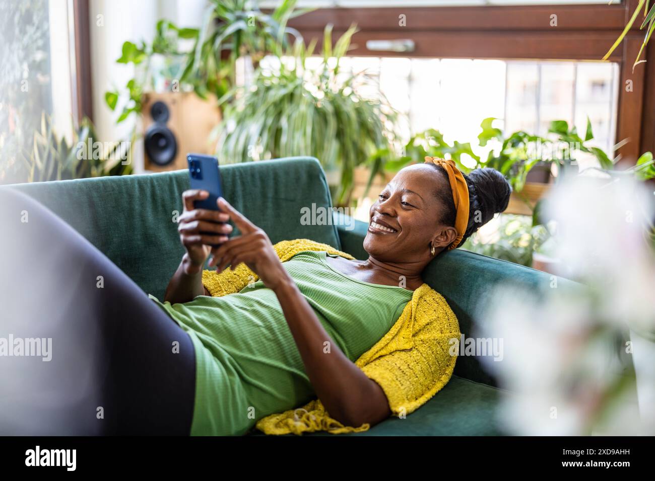 Woman using smartphone while relaxing on sofa at home Stock Photo