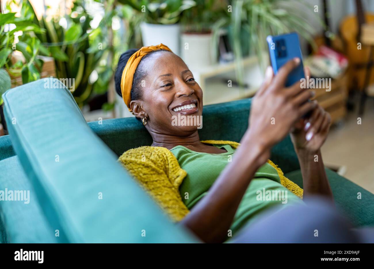 Woman using smartphone while relaxing on sofa at home Stock Photo
