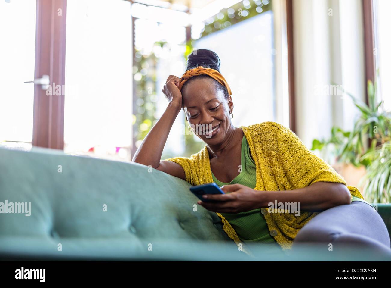 Woman using smartphone while relaxing on sofa at home Stock Photo