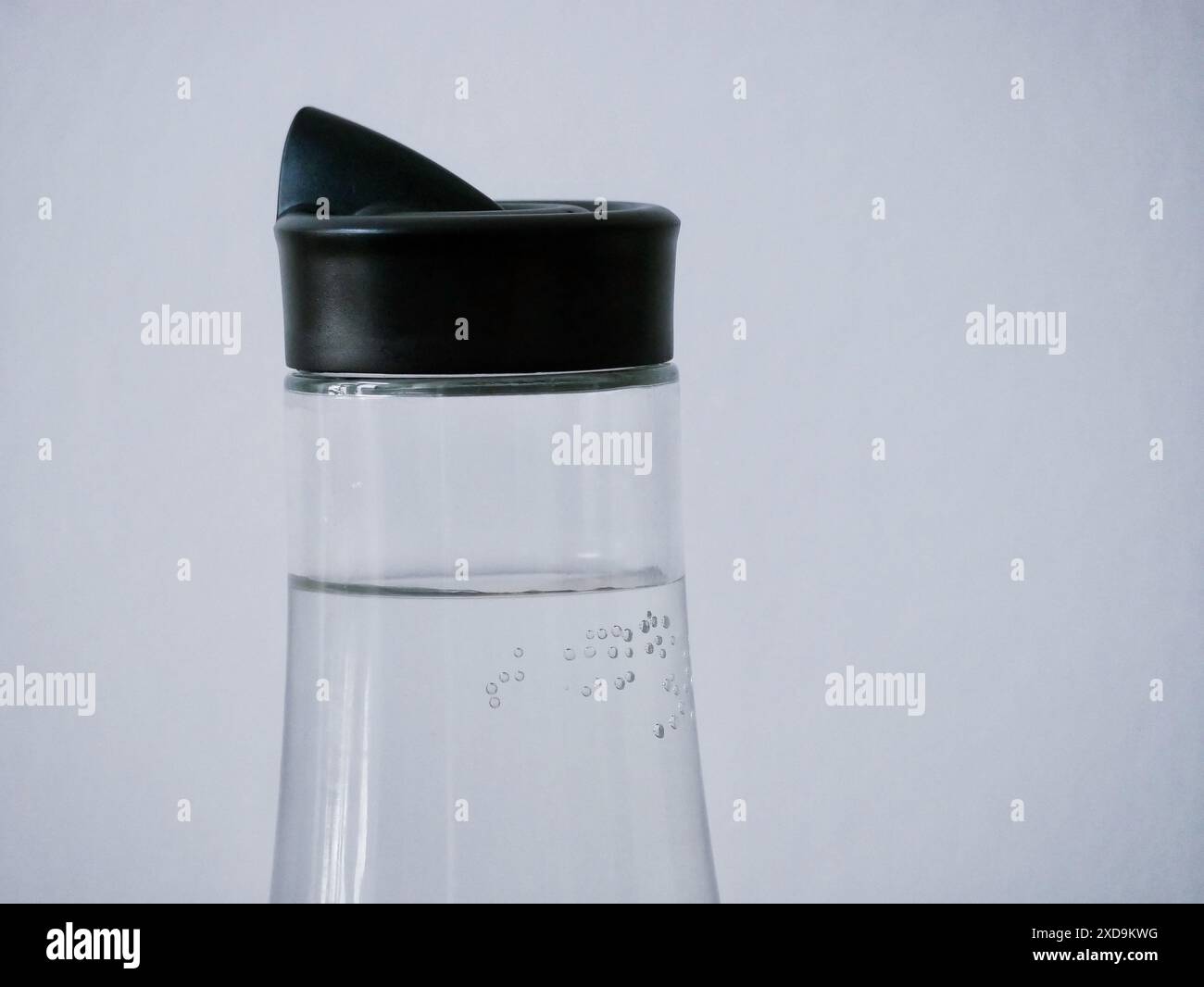 Glass bottle with water on a white background close-up. Air bubbles in water on the wall of the carafe. Stock Photo