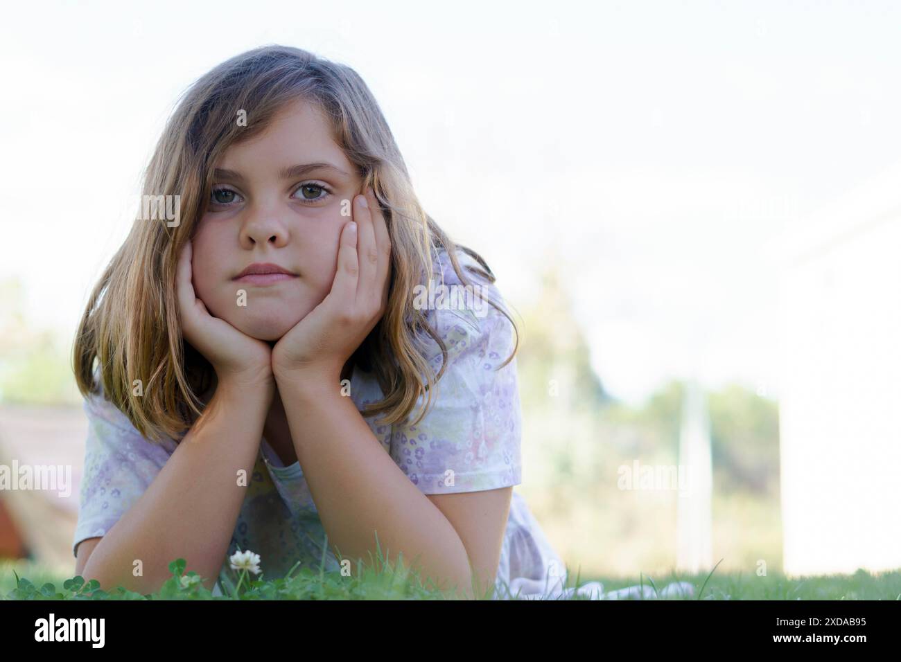 Portrait of a beautiful girl in a colorful dress lying on the grass looking at the camera with a white background and copy space Stock Photo